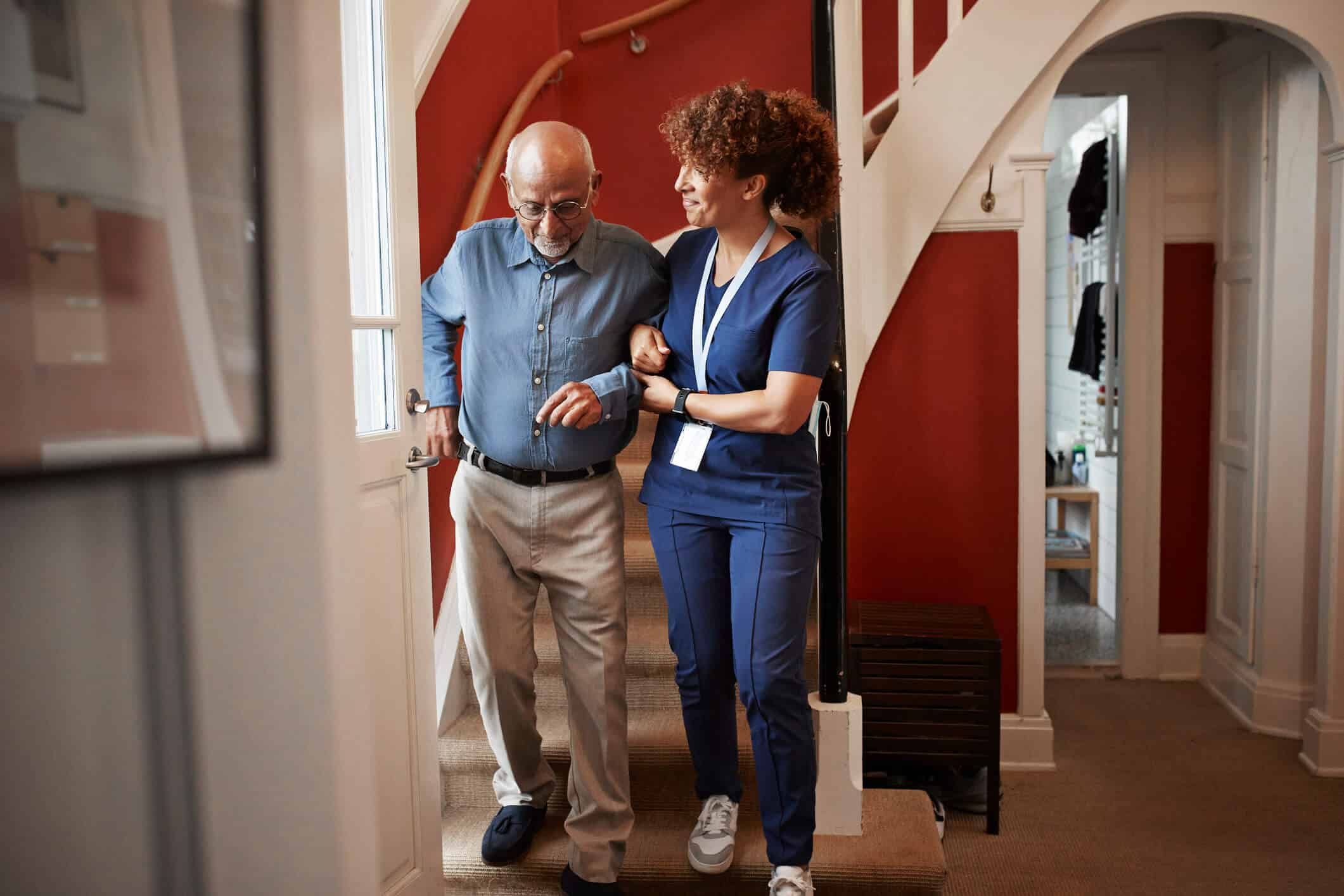 A woman holding an older mans arm while walking down the stairs.