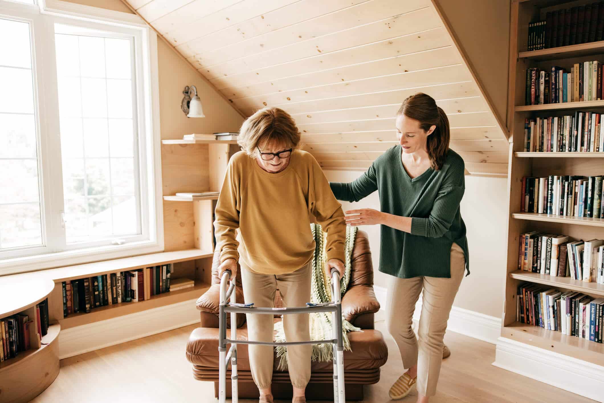 A woman assisting an older woman that is using a walker.